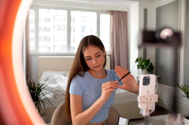 A close-up shot of a micro-influencer filming a live video review of a skincare product in their home. Natural light fills the room, and the background is slightly blurred to keep the focus on the influencer and the product. Various skincare products from different brands are visible on a shelf in the background, lending credibility and context to the scene.