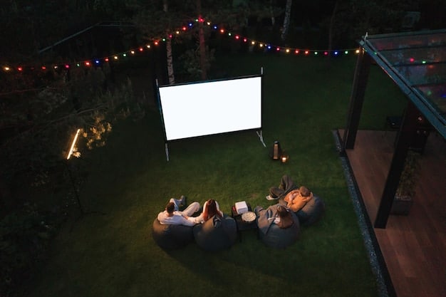 An overhead shot of a cozy outdoor movie setup at night. A projector screen displays a classic movie scene, lit by surrounding string lights. The seating area includes comfy cushions, blankets, and a small table with snacks and drinks.
